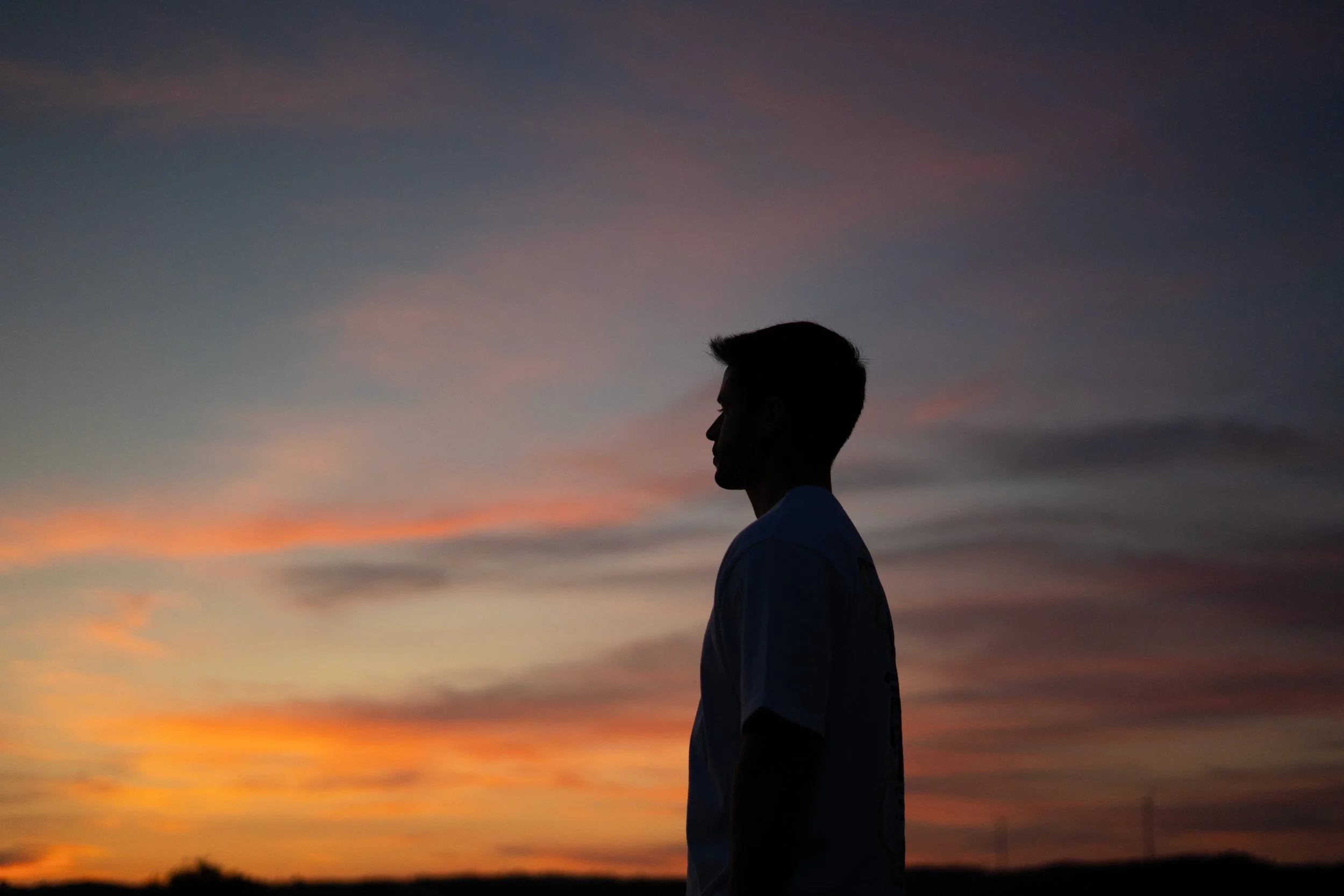 Silhouette of a person with short hair standing against a colorful sunset sky.