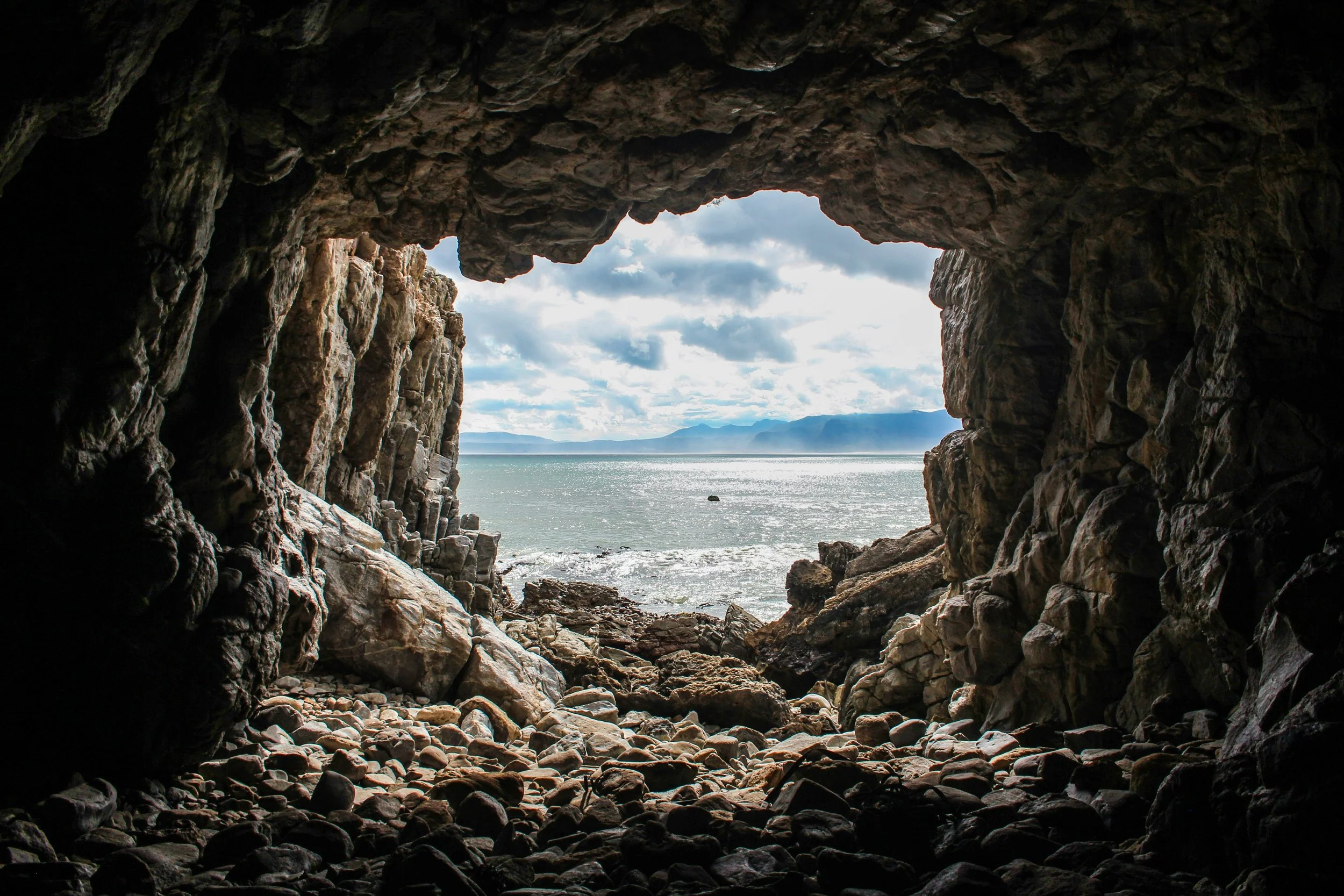 View from inside a rocky cave looking out towards the ocean with cloudy sky.