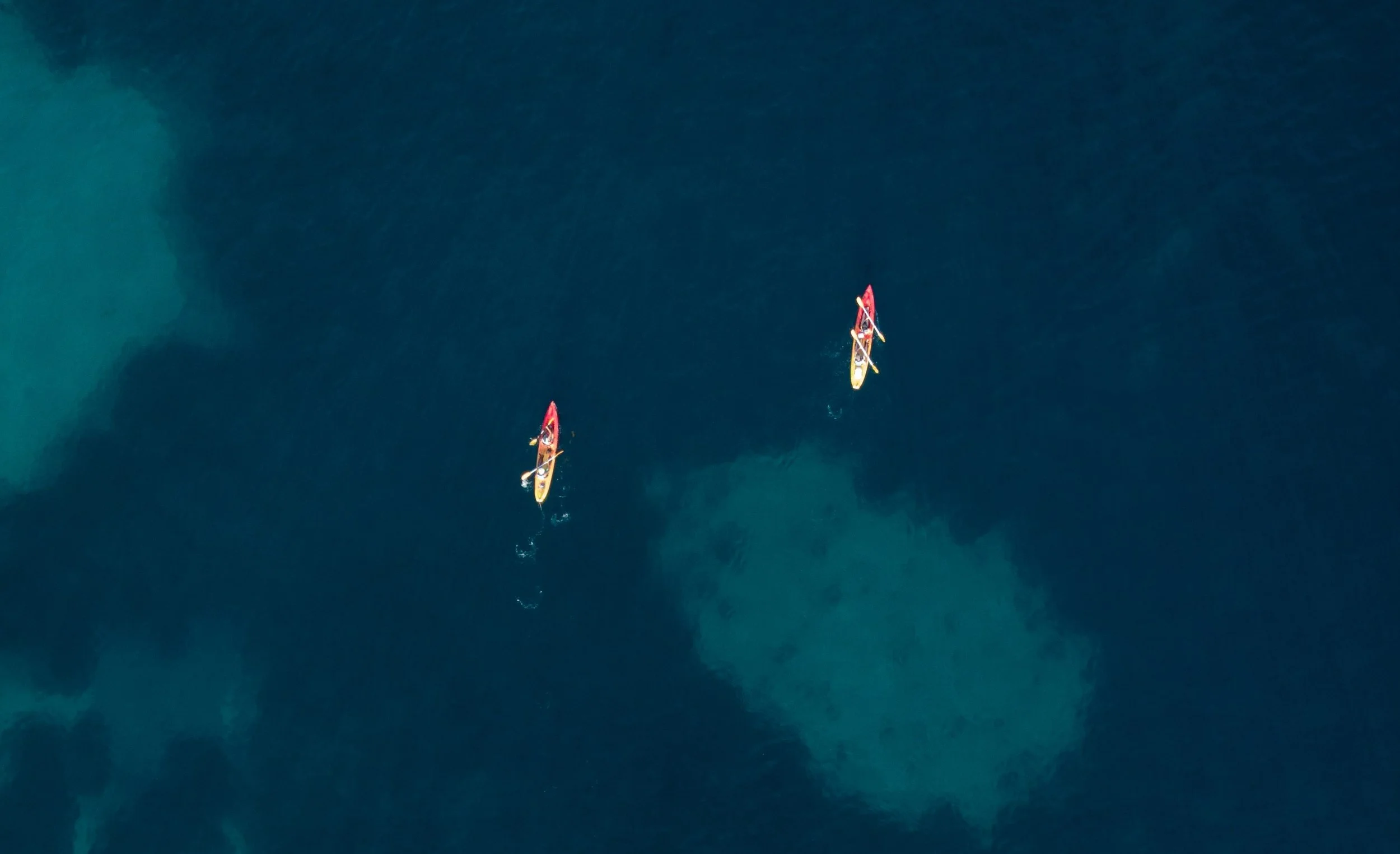 Two people kayak on a dark blue ocean.
