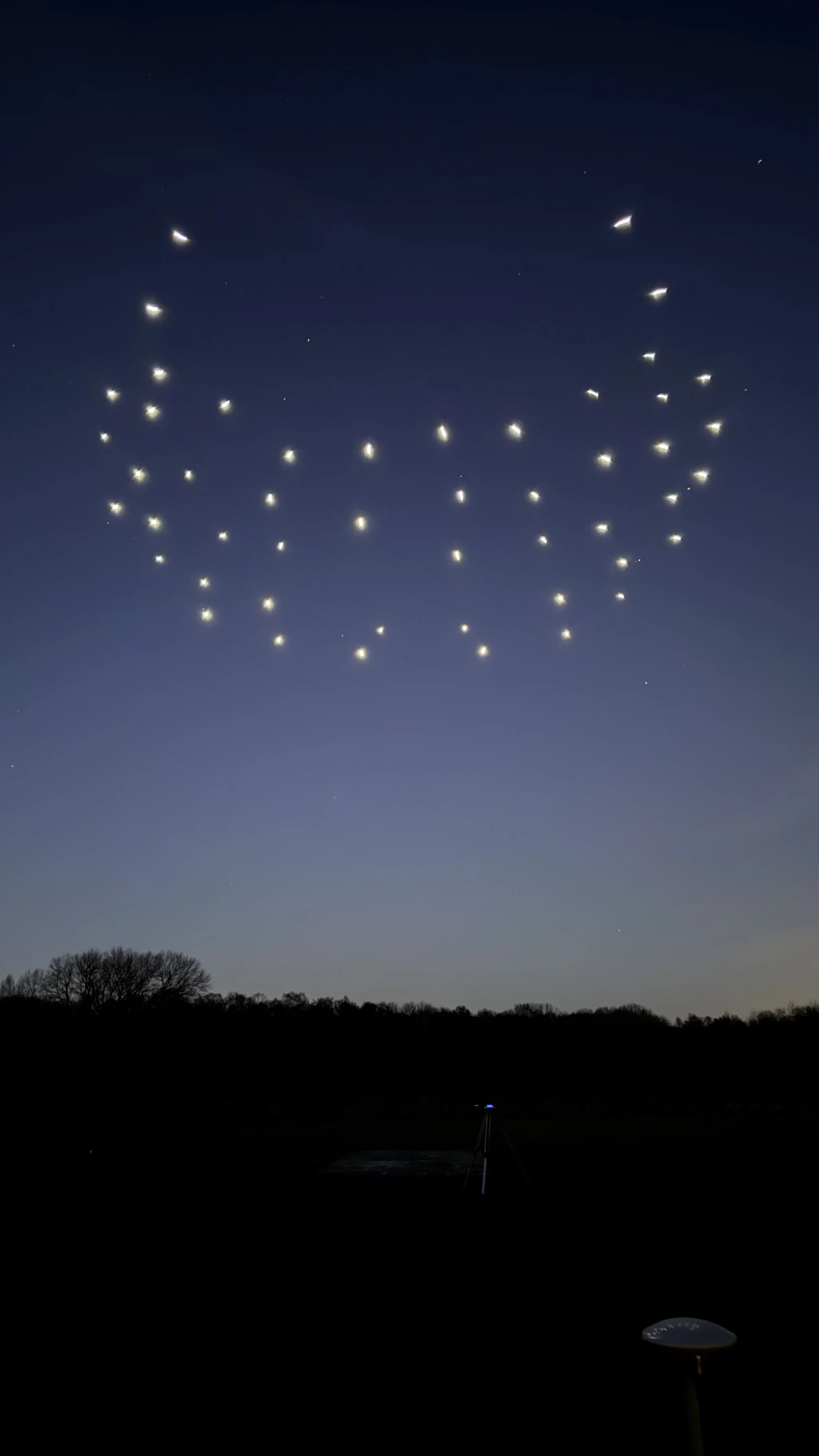 Night sky with multiple small lights, possibly drones, forming a shape.