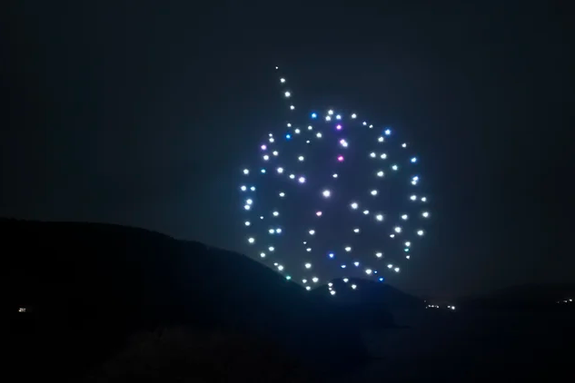 Drone light show in the night sky above a dark landscape.