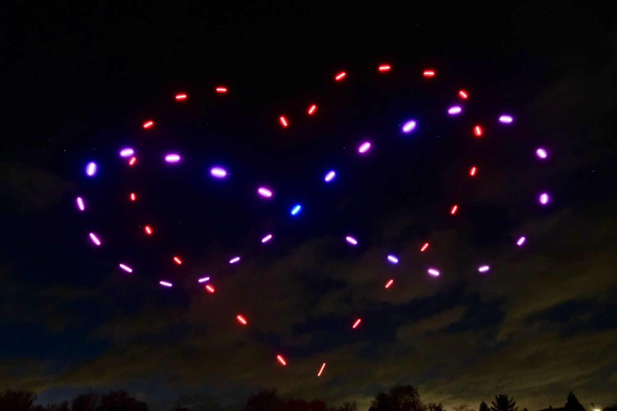 Night sky with colorful drone light display forming infinity symbol.