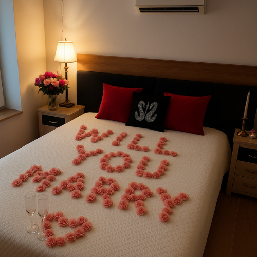 A bedroom with a bed decorated with pink roses spelling out "Will you marry me?" and a heart shape. There are two pillows, one black with a silver "love" symbol and two red pillows. A nightstand with a lamp and a vase of flowers is beside the bed, wi