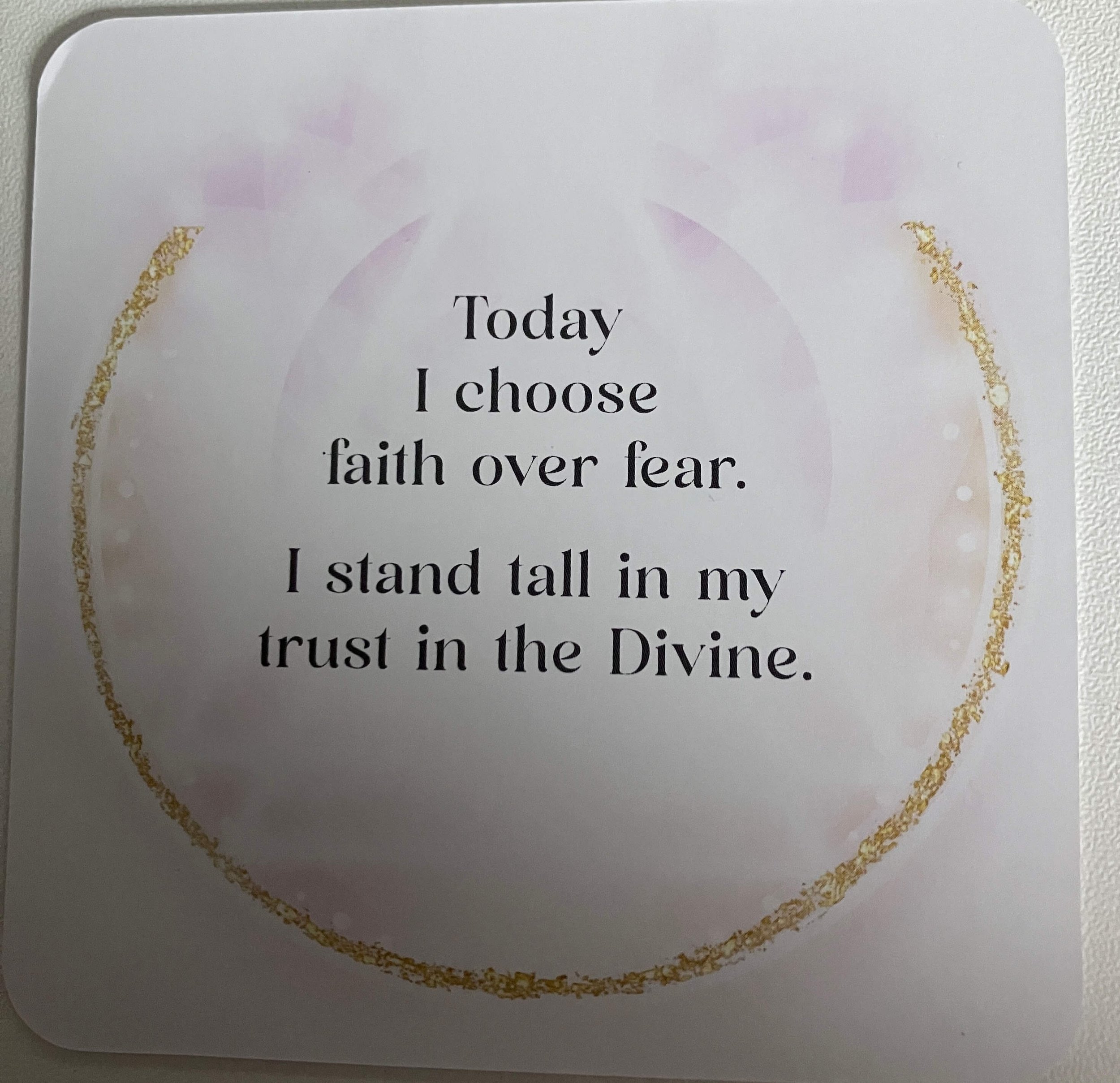 An inspirational quote on a white card with a gold circular border and soft pastel accents. The quote reads: "Today I choose faith over fear. I stand tall in my trust in the Divine."