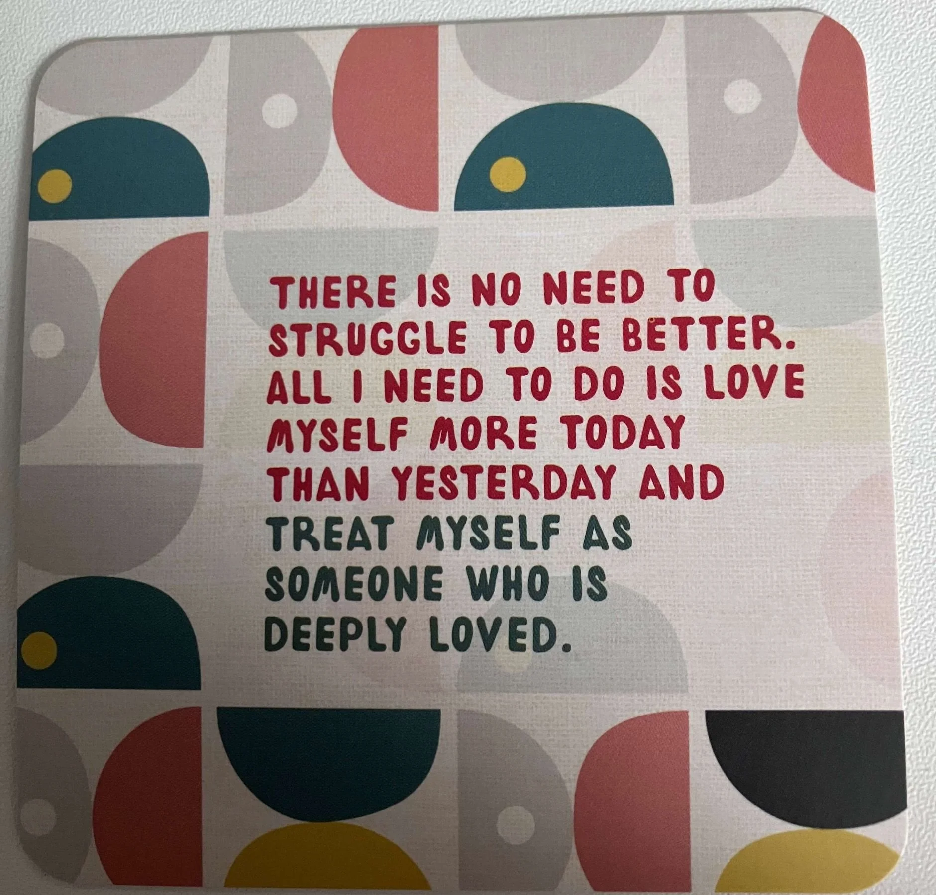 A decorative wall poster with an inspirational quote. The quote says, 'There is no need to struggle to be better. All I need to do is love myself more today than yesterday and treat myself as someone who is deeply loved.' The background features abstract shapes in red, yellow, black, beige, and teal.