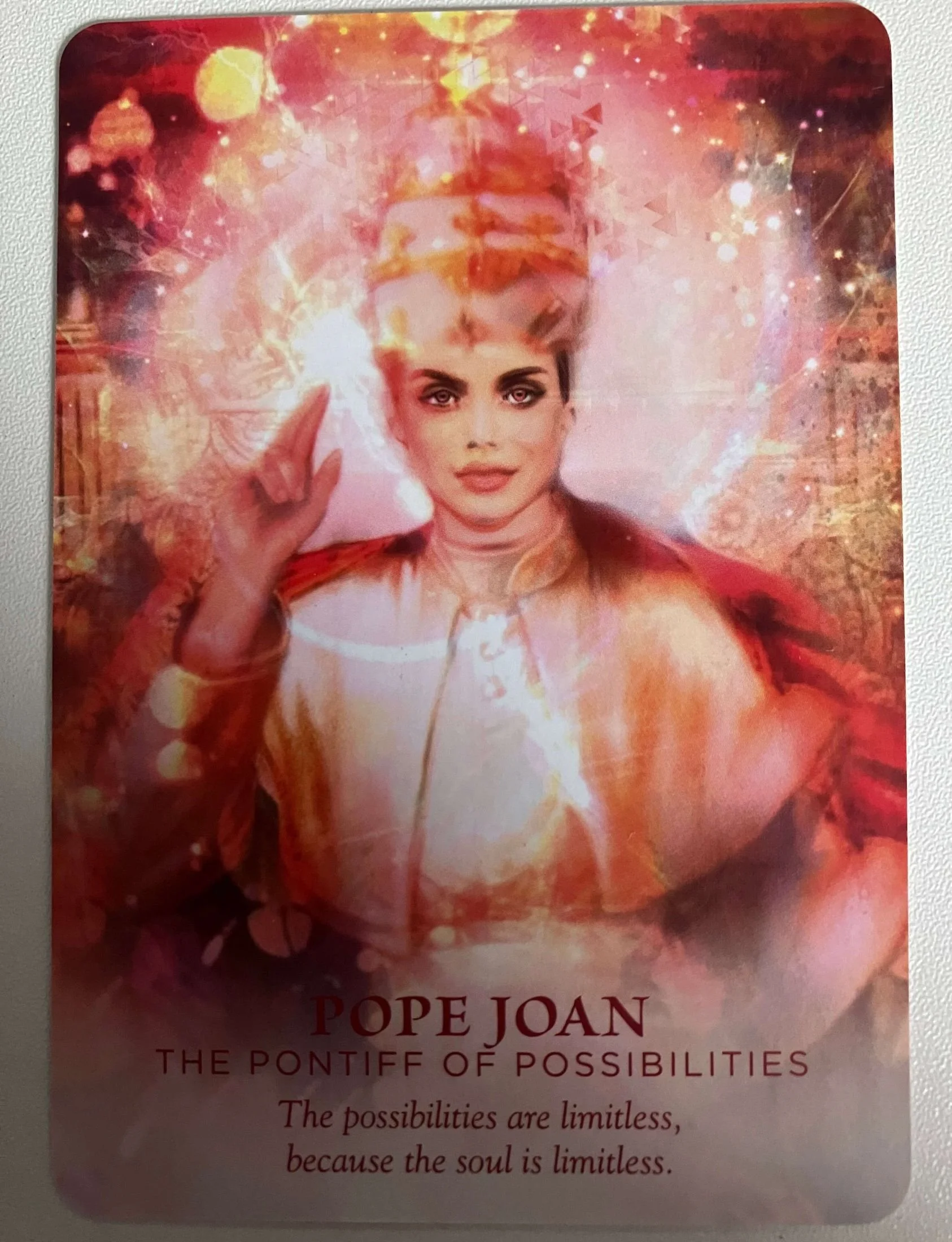 A digitally manipulated image of a woman with styled hair and makeup, wearing a regal outfit. The background is a mix of pink, orange, and white with abstract glowing elements and sparkles. Text reads: 'Pope Joan, The Pontiff of Possibilities, The possibilities are limitless, because the soul is limitless.'
