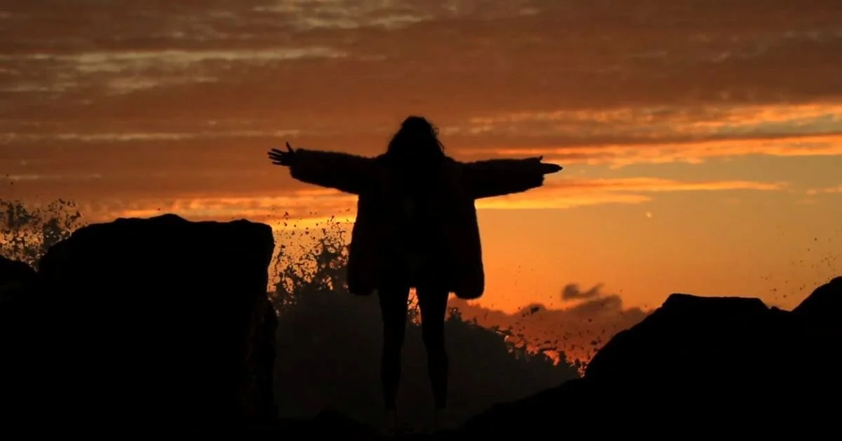 Woman with arms outstreched at sunset on a rocky shoreline.jpg