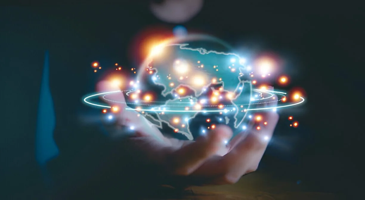 Hand holding a glowing digital globe with orbiting lines and light points on a dark background.