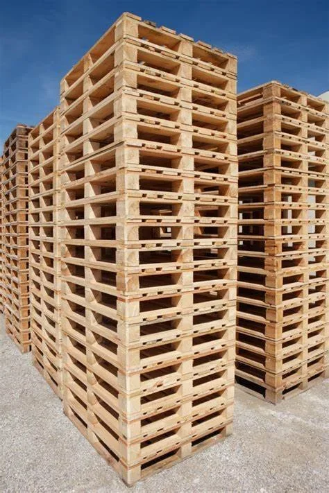Several stacks of wooden pallets stored outdoors on a gravel surface under a clear blue sky.