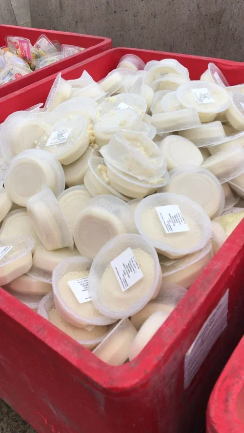 Large red bin filled with pre-packaged blocks of cheese with white labels.