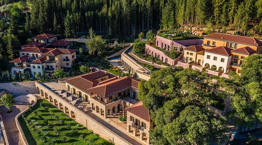 Aerial view of a luxurious hillside residential community with Mediterranean-style houses, surrounded by lush trees and forest in the background.