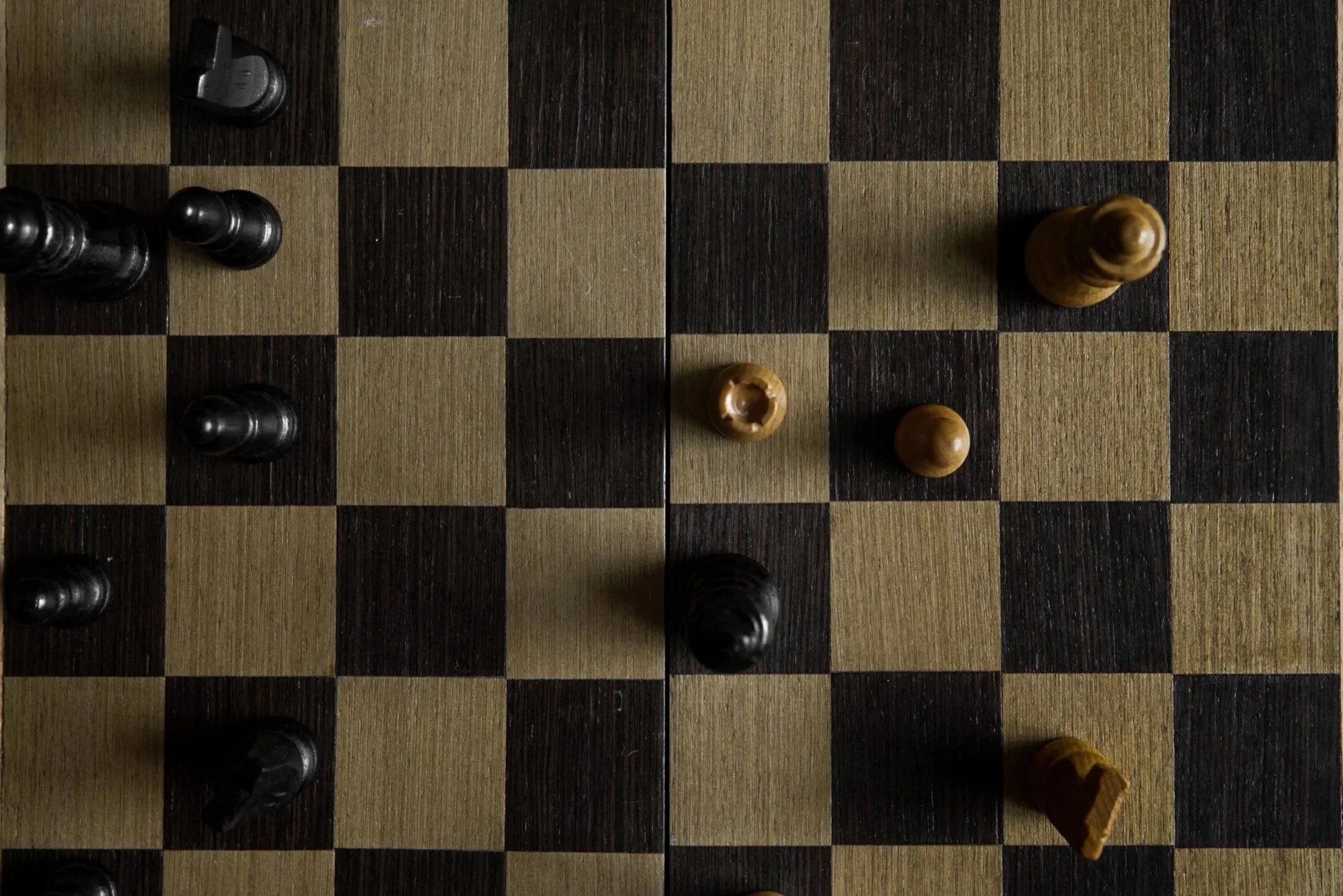 An overhead view of a chessboard with black and brown chess pieces arranged on the squares.