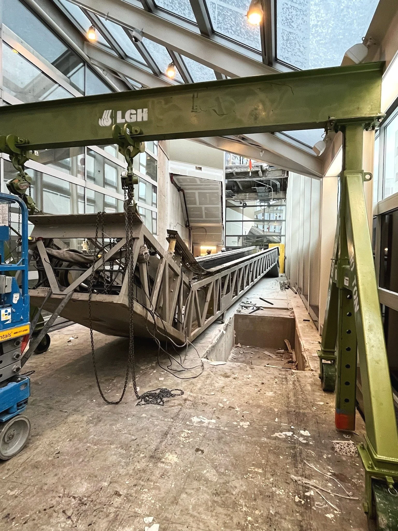 Construction site with a large green crane and a fallen ladder inside a building with glass ceiling