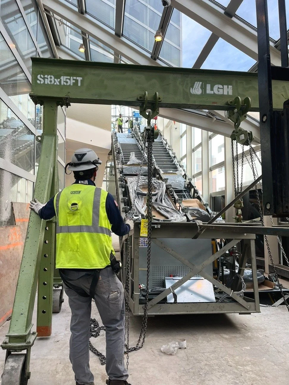 Construction worker in safety vest and helmet standing near a large green crane, working inside a building at Denver Center for the Performing Arts - completed by FH Construction Group.
