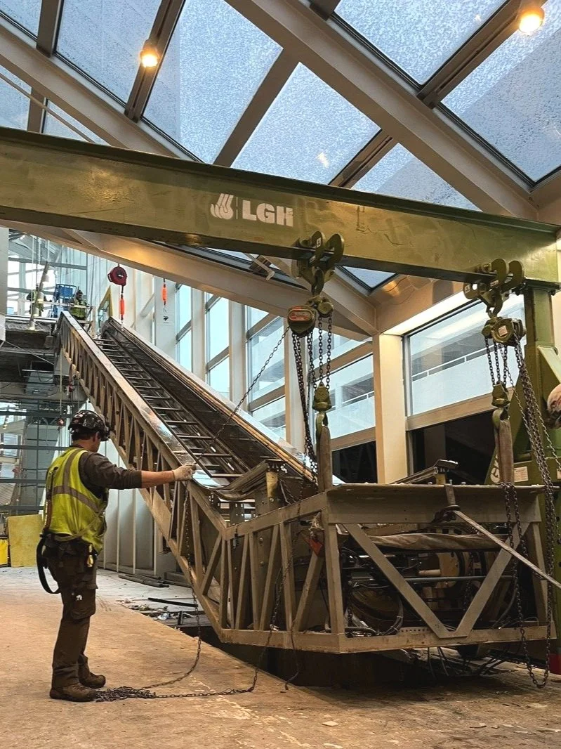 Construction worker in safety vest and helmet inspecting a large steel structure with a steep inclined ramp inside a building with a glass ceiling at Denver Center for the Performing Arts renovation project completed by FH Construction Group.