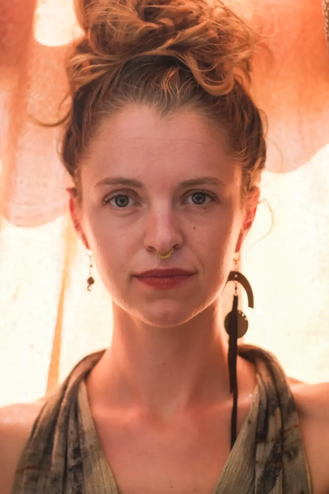 Verena Franzetti vue de face portant une robe avec des boucles d'oreilles avec des rideaux au fond 