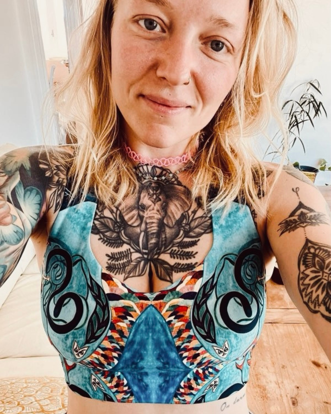 Une femme souriante avec de nombreux tatouages sur le torse et les bras pose pour une photo en intérieur.