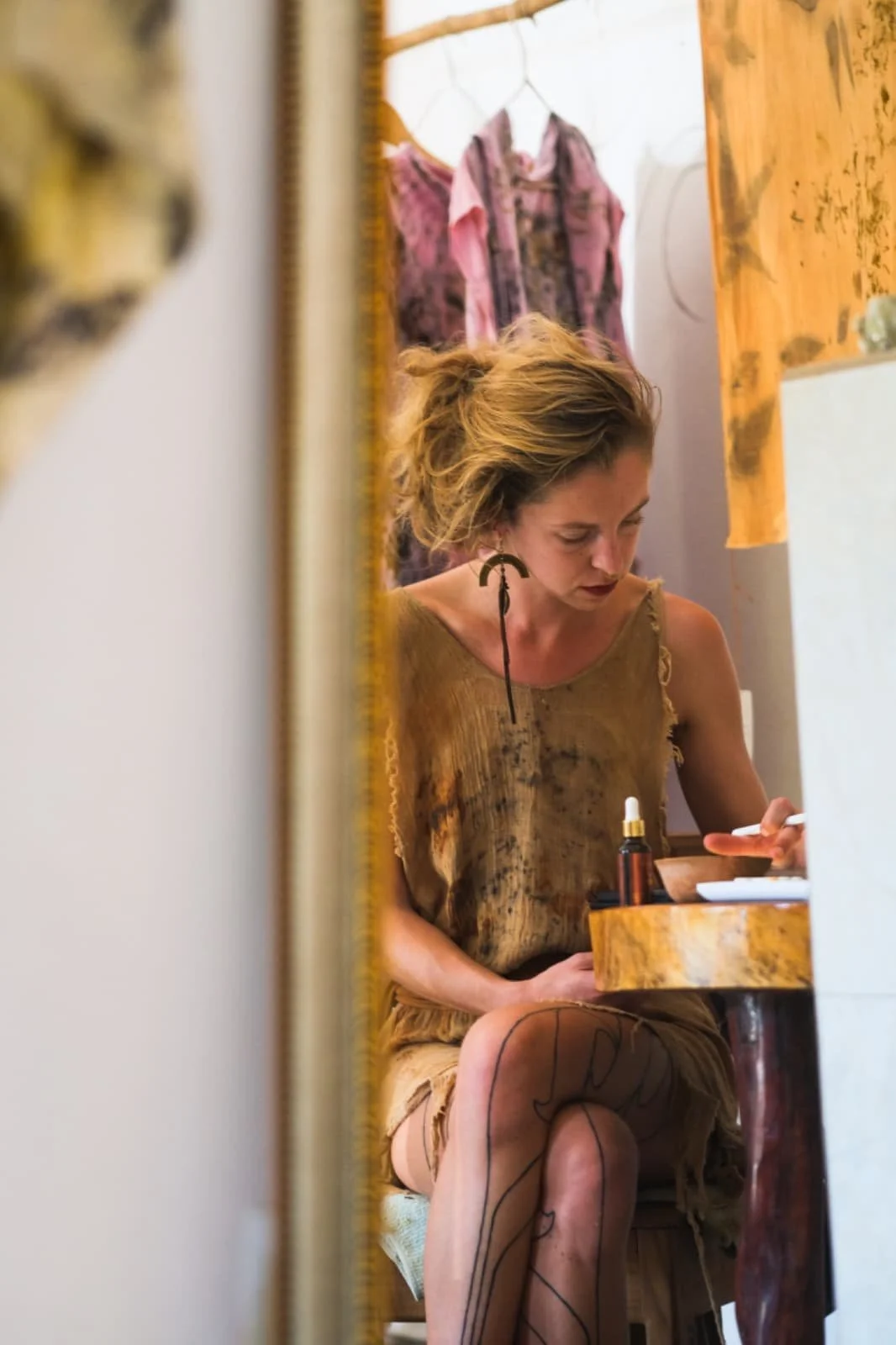 Verena Franzetti portant une robe beige est assise à un bureau dessinant. Atelier d'artiste 