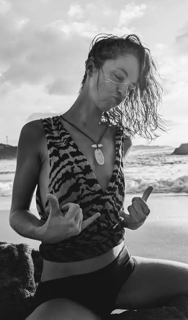 Verena Franzetti à genoux sur une plage,faisant un signe avec ces deux mains, en noir et blanc.
