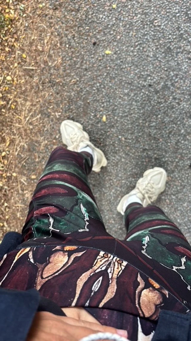 Prise de vue en plongée montrant des jambes avec des vêtements colorés et des chaussures blanches, marchant sur une route en partie goudronnée et en partie herbeuse.