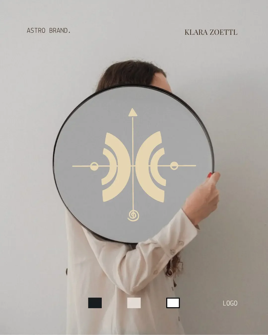 Une personne tient une plaque ronde avec un design graphique et en haut à gauche écrit 'ASTRO BRAND' et en haut à droite 'KLARA ZOETTL'. La plaque masque partiellement le visage de la personne.