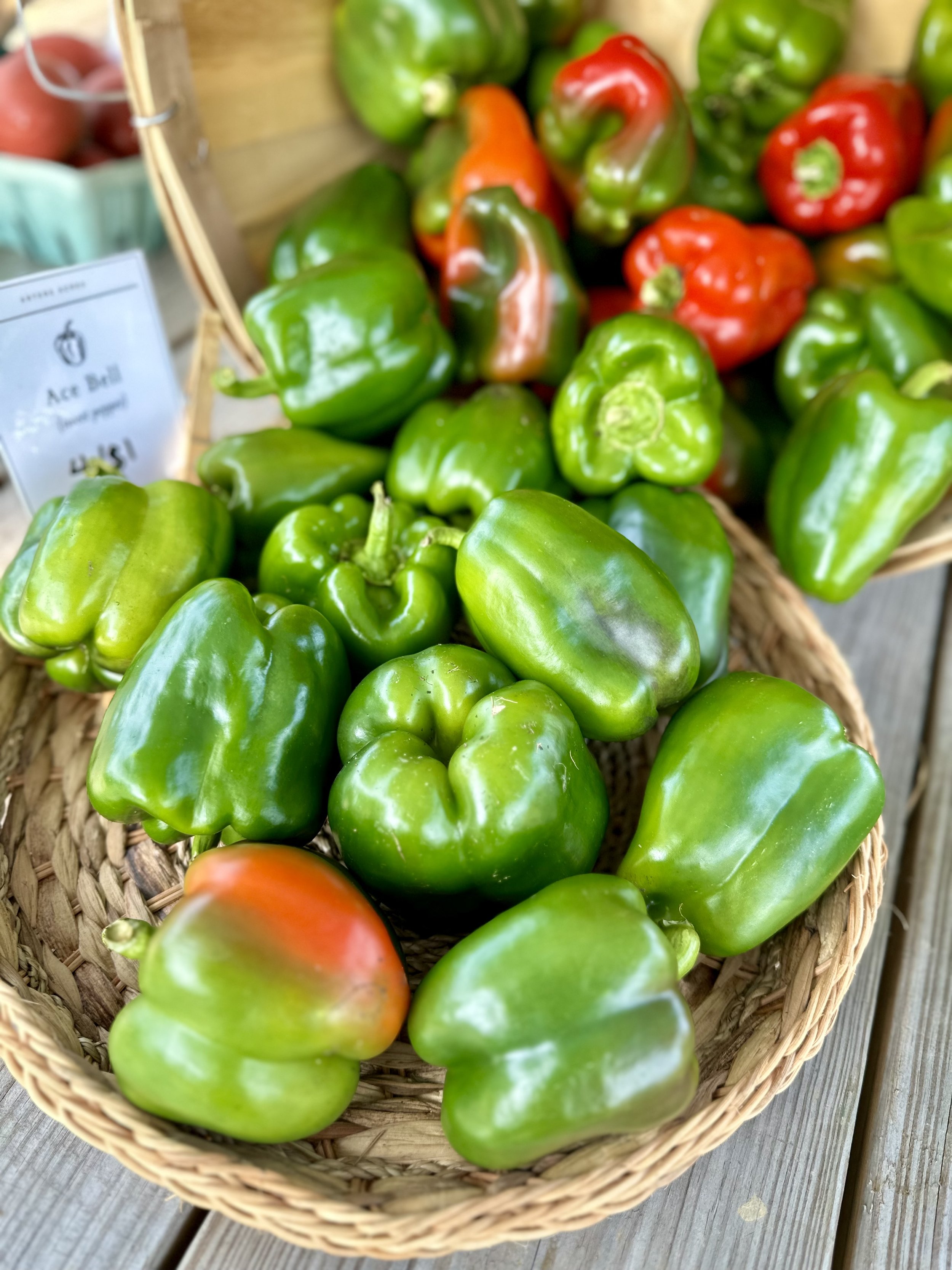 Green and red bell peppers in a wicker basket on a wooden surface.
