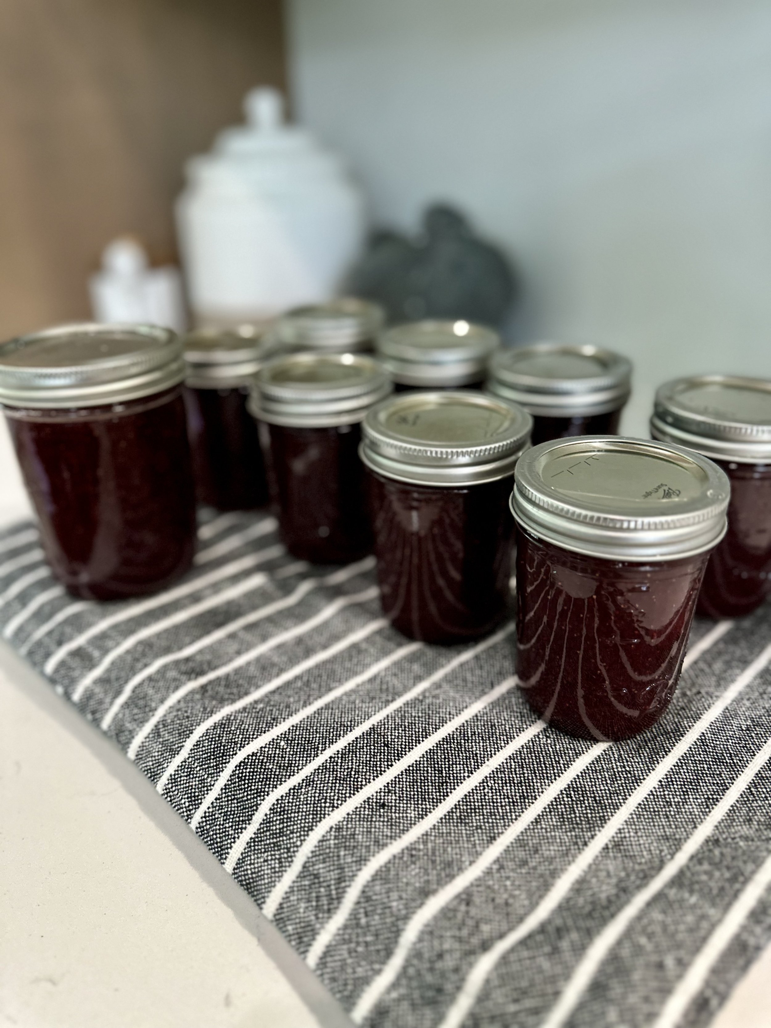 Glass jars filled with dark red jam on a black and white striped cloth.