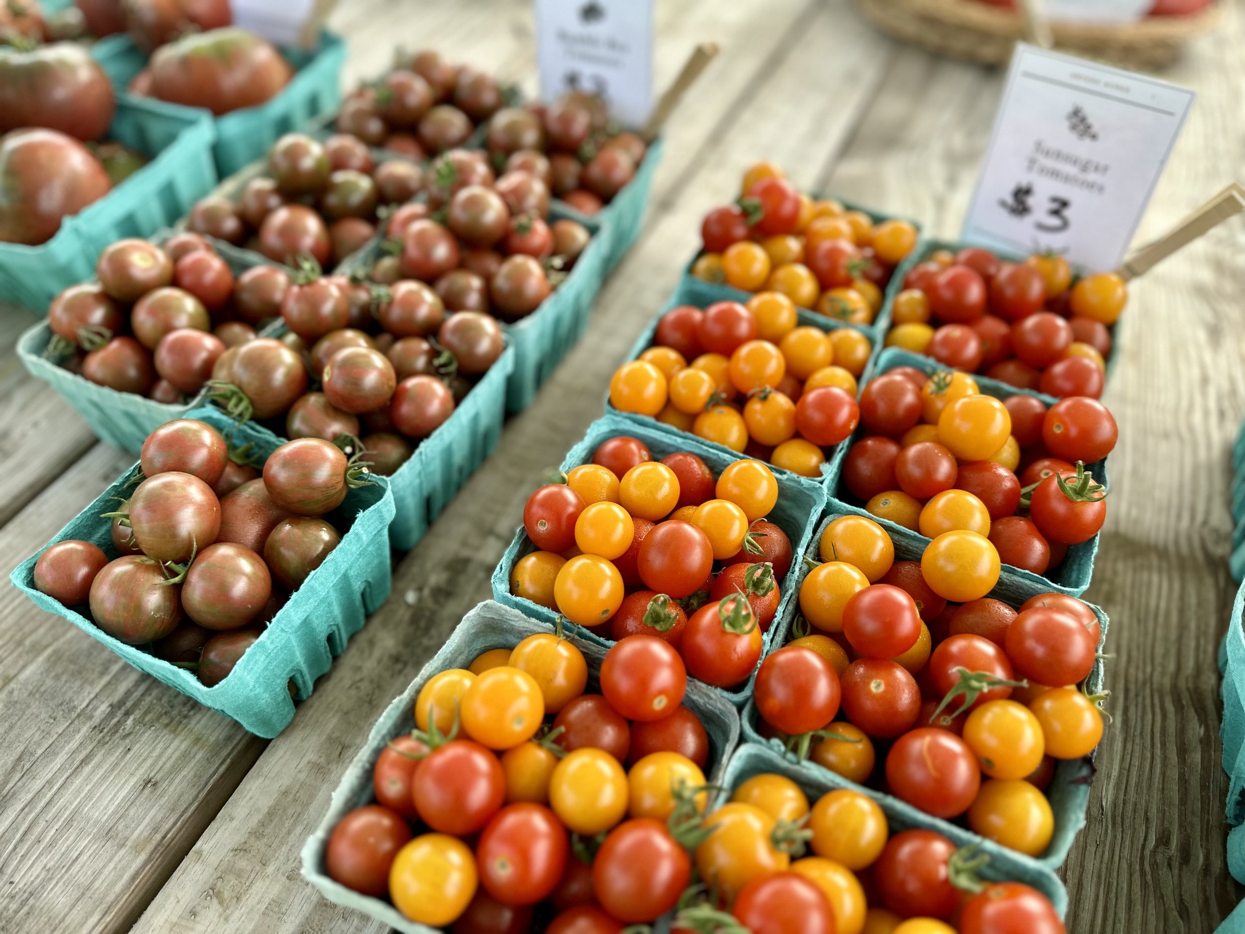 Various cherry tomatoes in blue cartons displayed on a wooden table at a market.