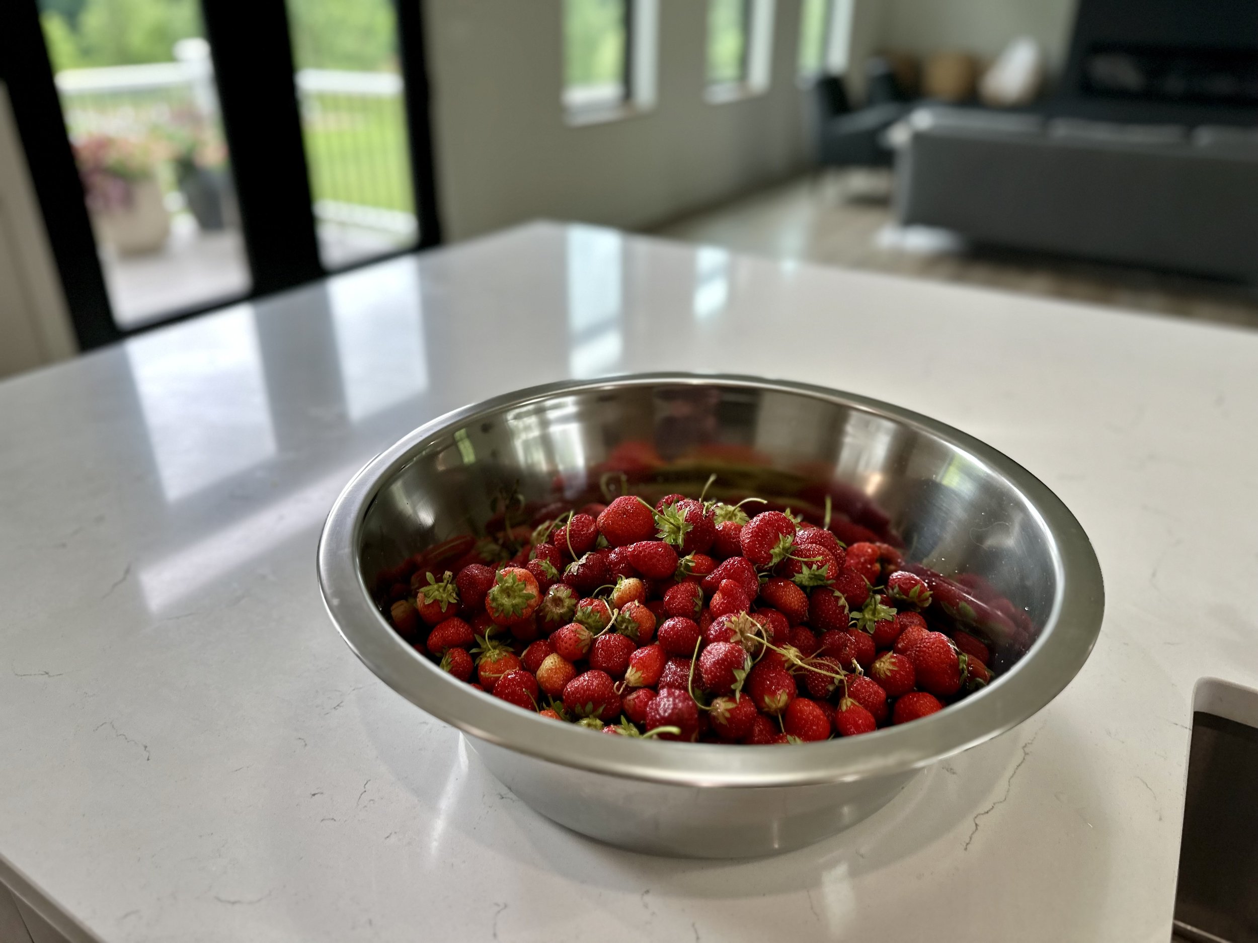 A large metal bowl filled with fresh strawberries on a kitchen counter.