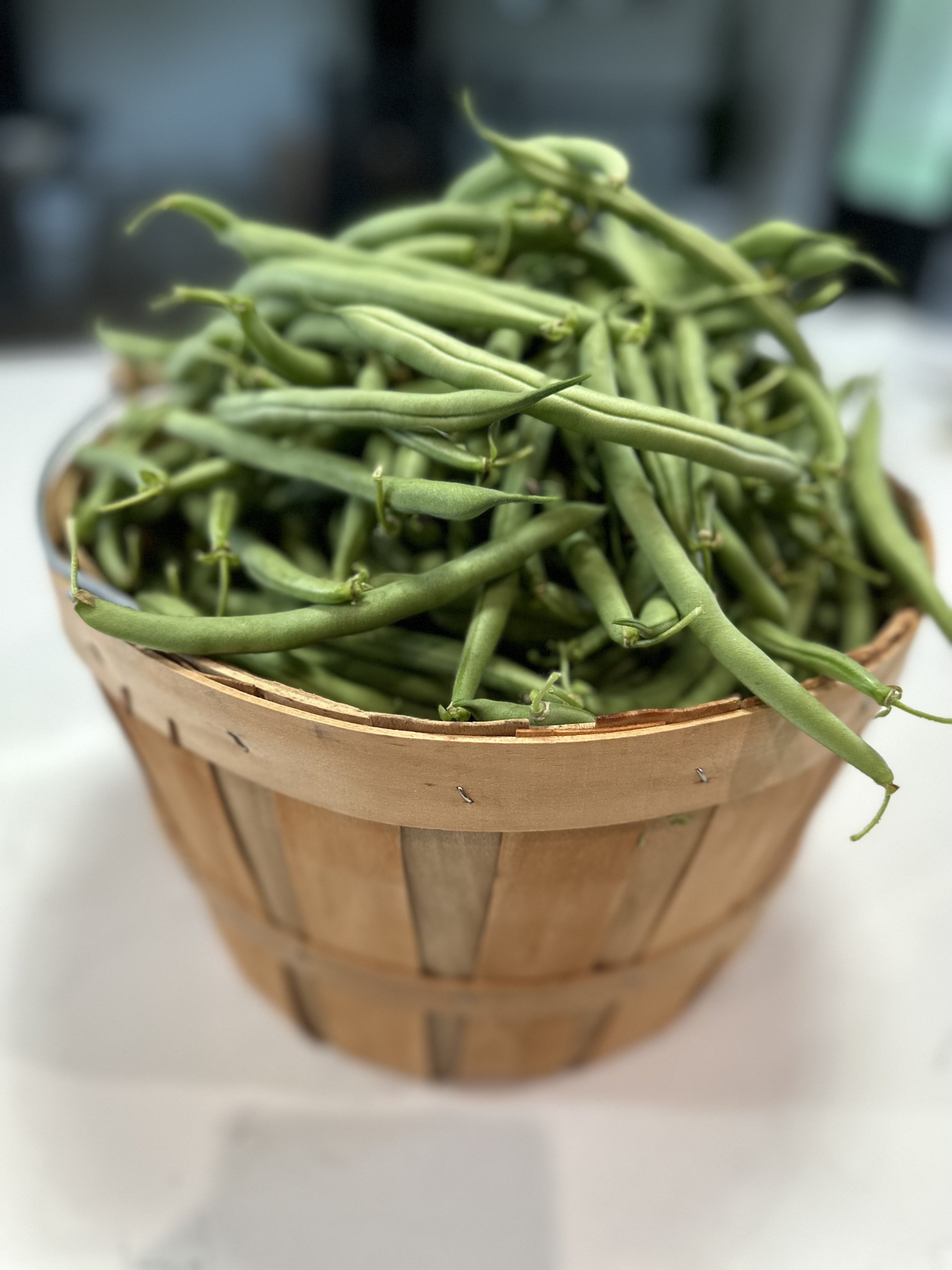 A wooden basket filled with fresh green beans.