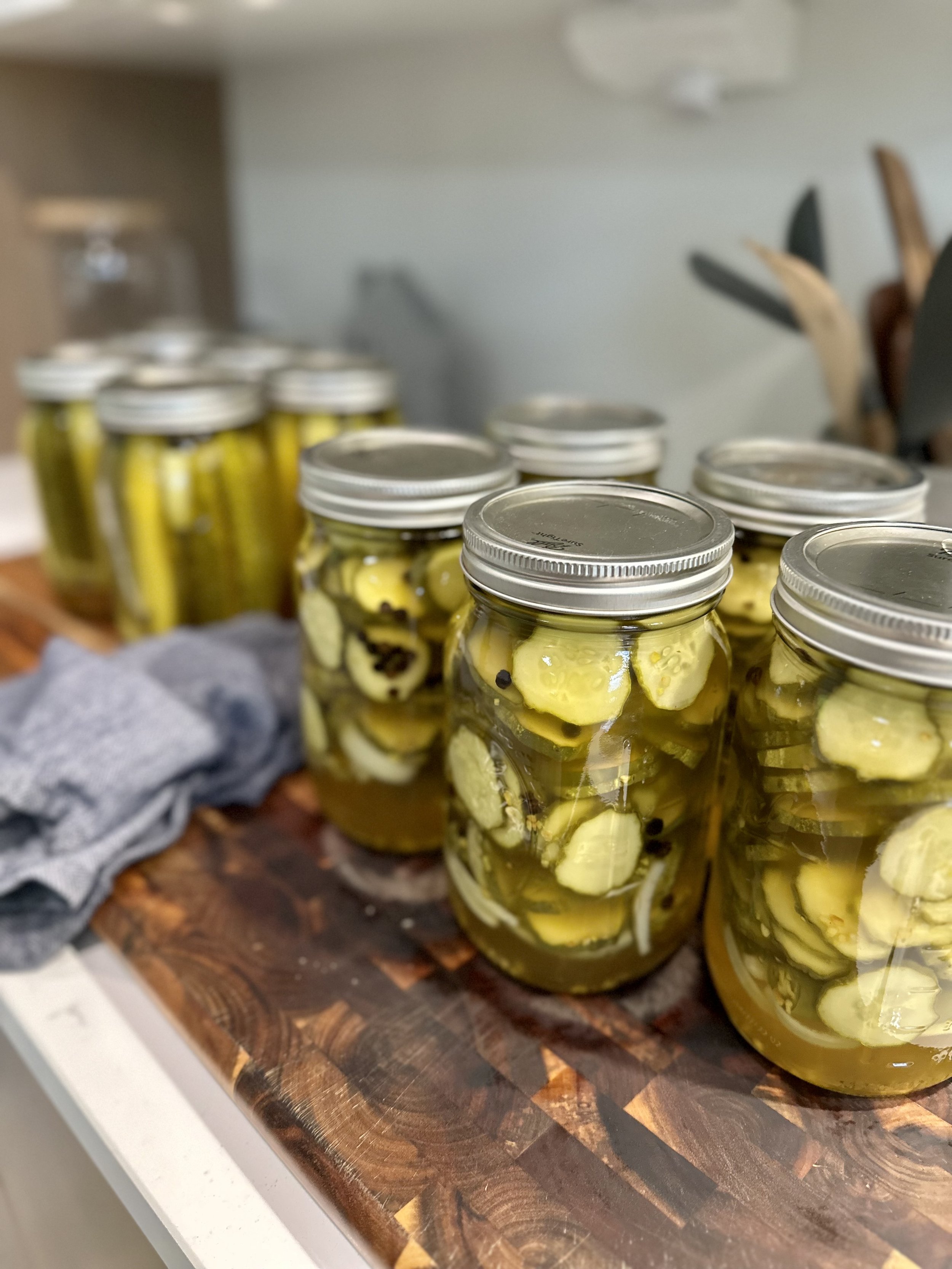 Mason jars filled with pickled cucumbers on a wooden cutting board, with some jars containing whole pickles and others with sliced pickles.