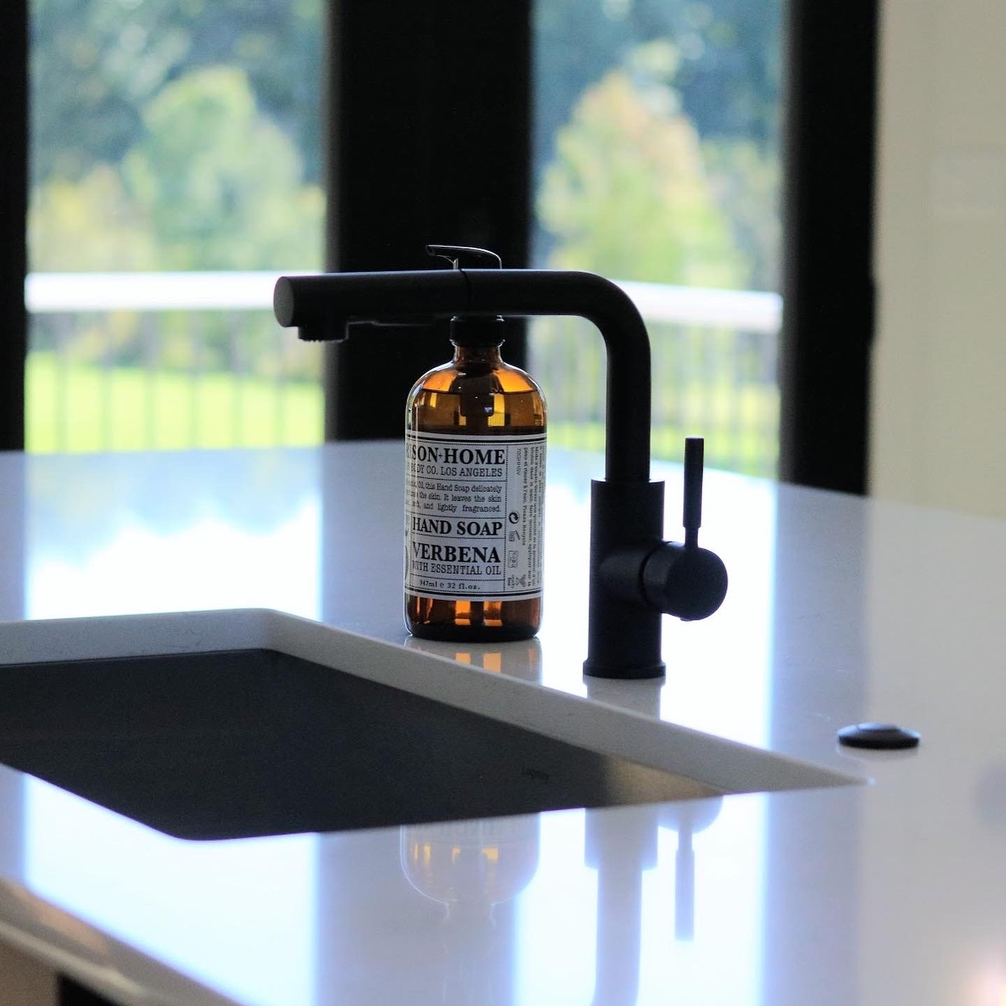 Modern kitchen sink with a black faucet and a bottle of hand soap on the counter.