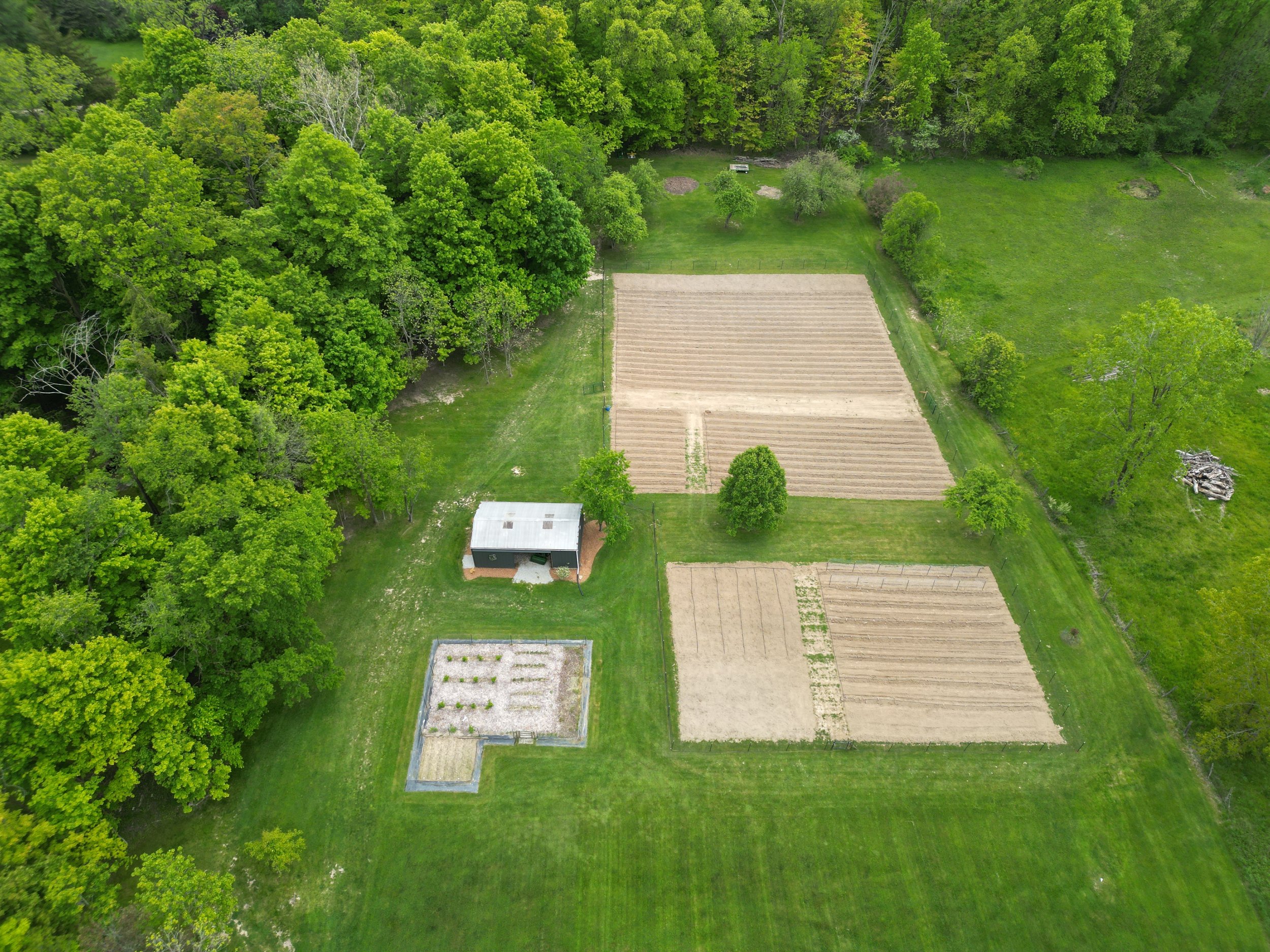 Aerial view of farmland with multiple plots and a small building surrounded by trees and green grass.