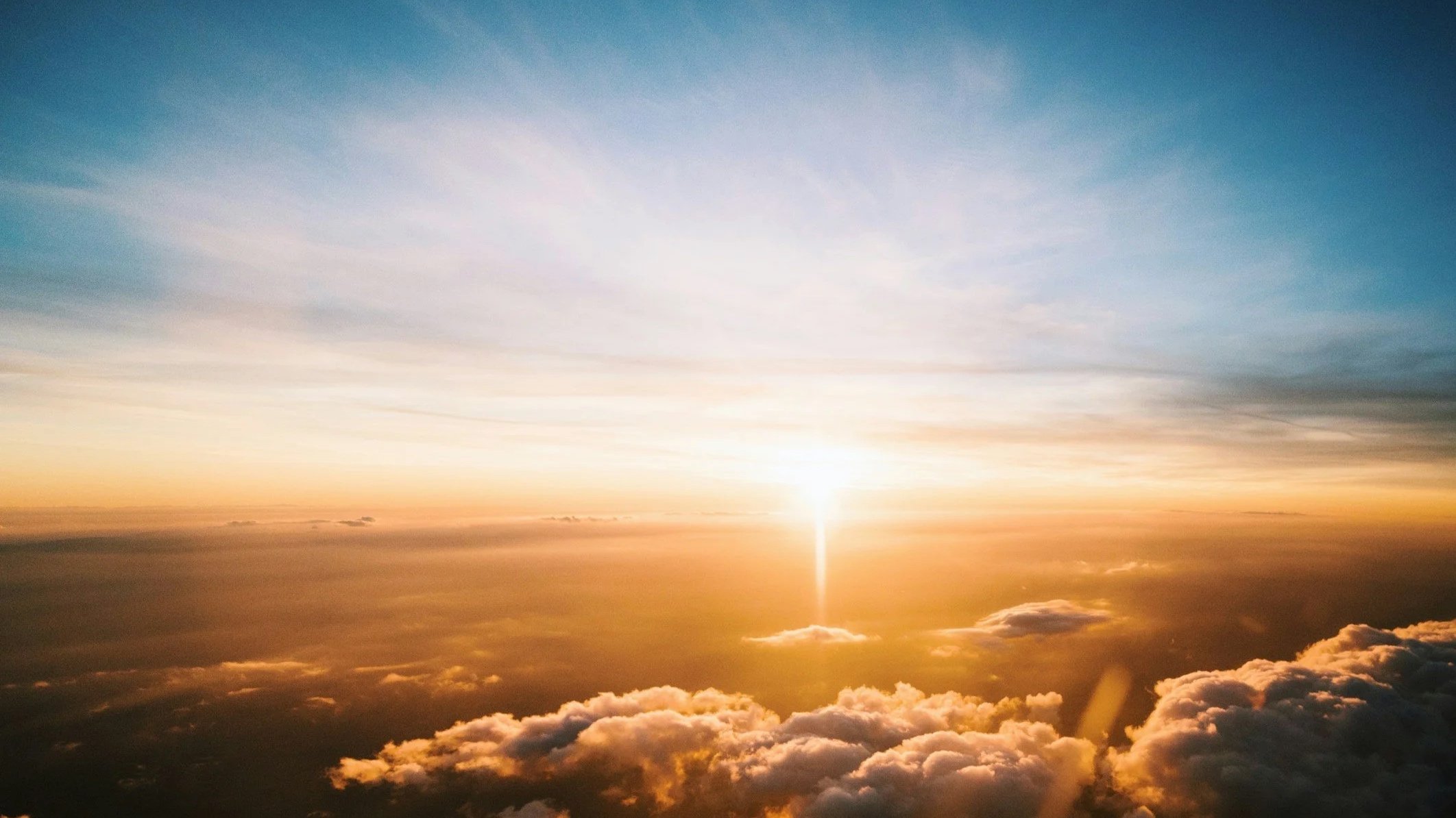 Amanecer con nubes doradas y cielo azul, vista desde la altura, con el sol en el horizonte.