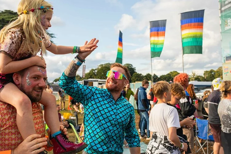 Festival-goers celebrating outdoors with family near boutique glamping village decorated with rainbow flags