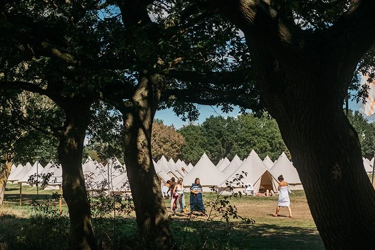 Festival guests walking through boutique glamping field surrounded by bell tents