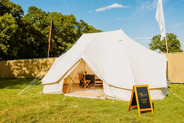 Pamper tent with open entrance, table and chairs inside, set on grass under blue skies — boutique camping setup for luxury outdoor stays
