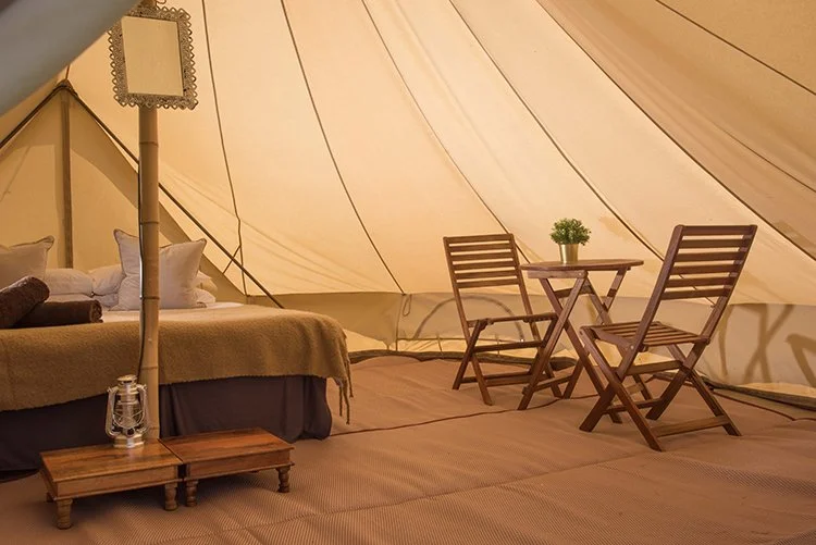 Super Bell tent interior with double bed, wooden furniture, and lantern in boutique glamping village