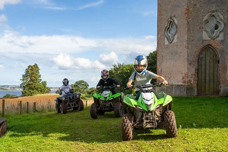 Children riding quad bikes near historic building at an outdoor glamping and boutique camping festival