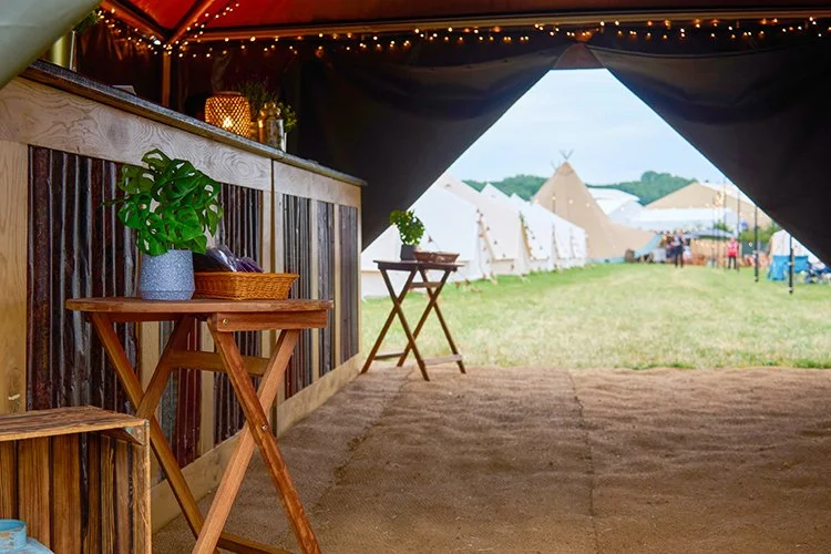 View from Hotel Bell Tent reception overlooking boutique glamping village with bell tents, tipis, string lights, and outdoor decor