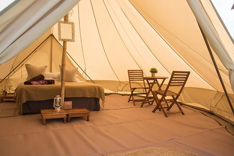 Super bell tent interior with soft bedding, lantern lighting, and wooden furniture creating a cosy boutique camping setup