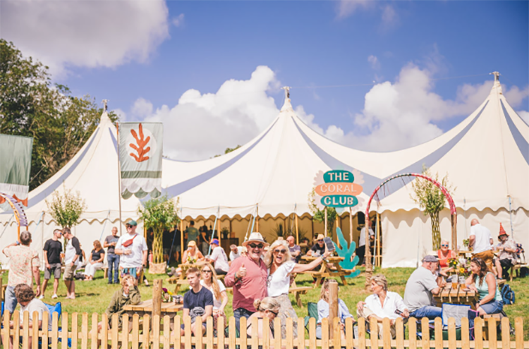 Festival guests gathering under decorated marquee tent with colorful banners at outdoor glamping event