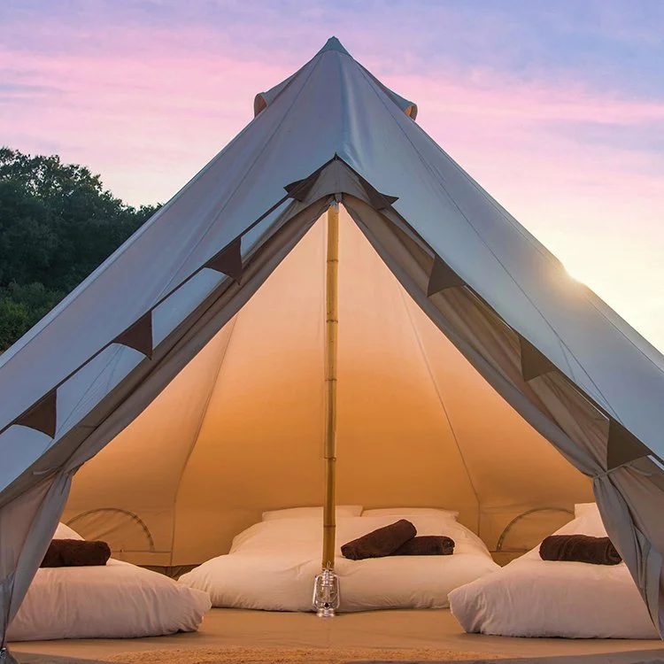 Luxury Classic Bell tent interior with warm lighting, soft bedding, and rolled towels at sunset beneath a pink and purple sky.