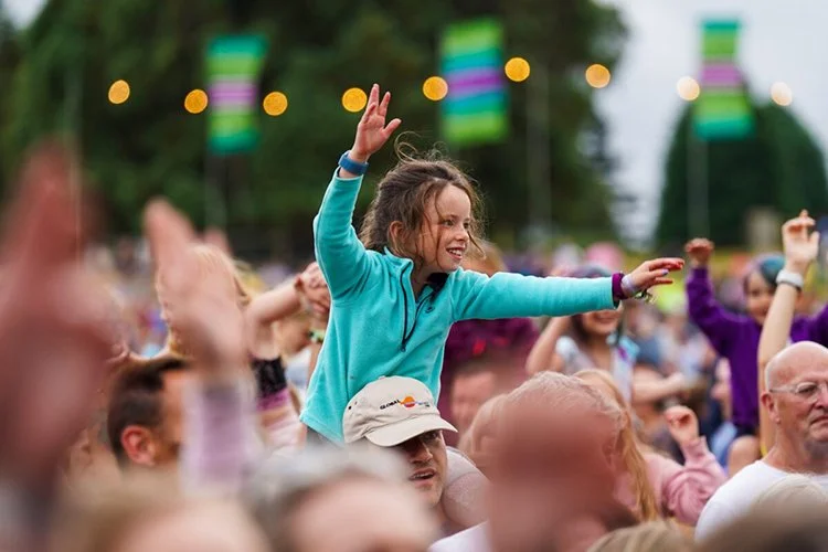 Festival guest enjoying live music at boutique glamping event with colorful lights and family-friendly atmosphere