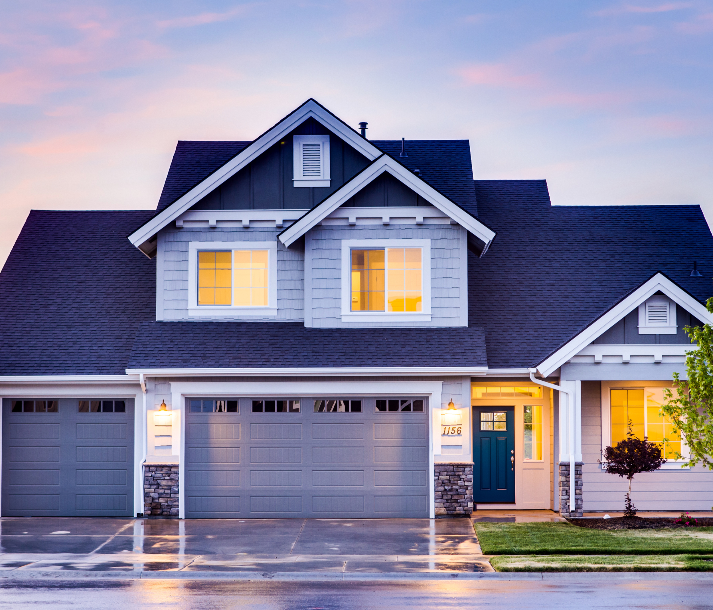 Storm-damaged modern two-story home in Columbus with wet roof and exterior lighting at dusk