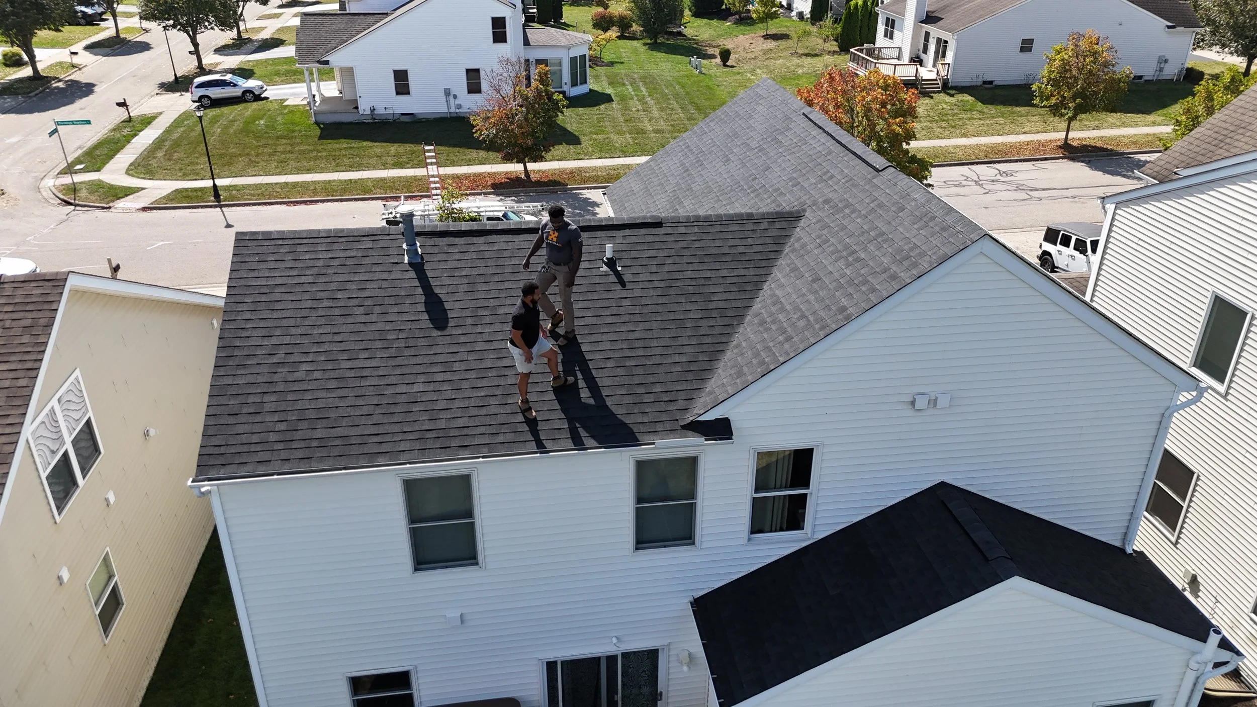 Two people on the roof of a white house, inspecting or working, with ROOFING MARYSVILLE