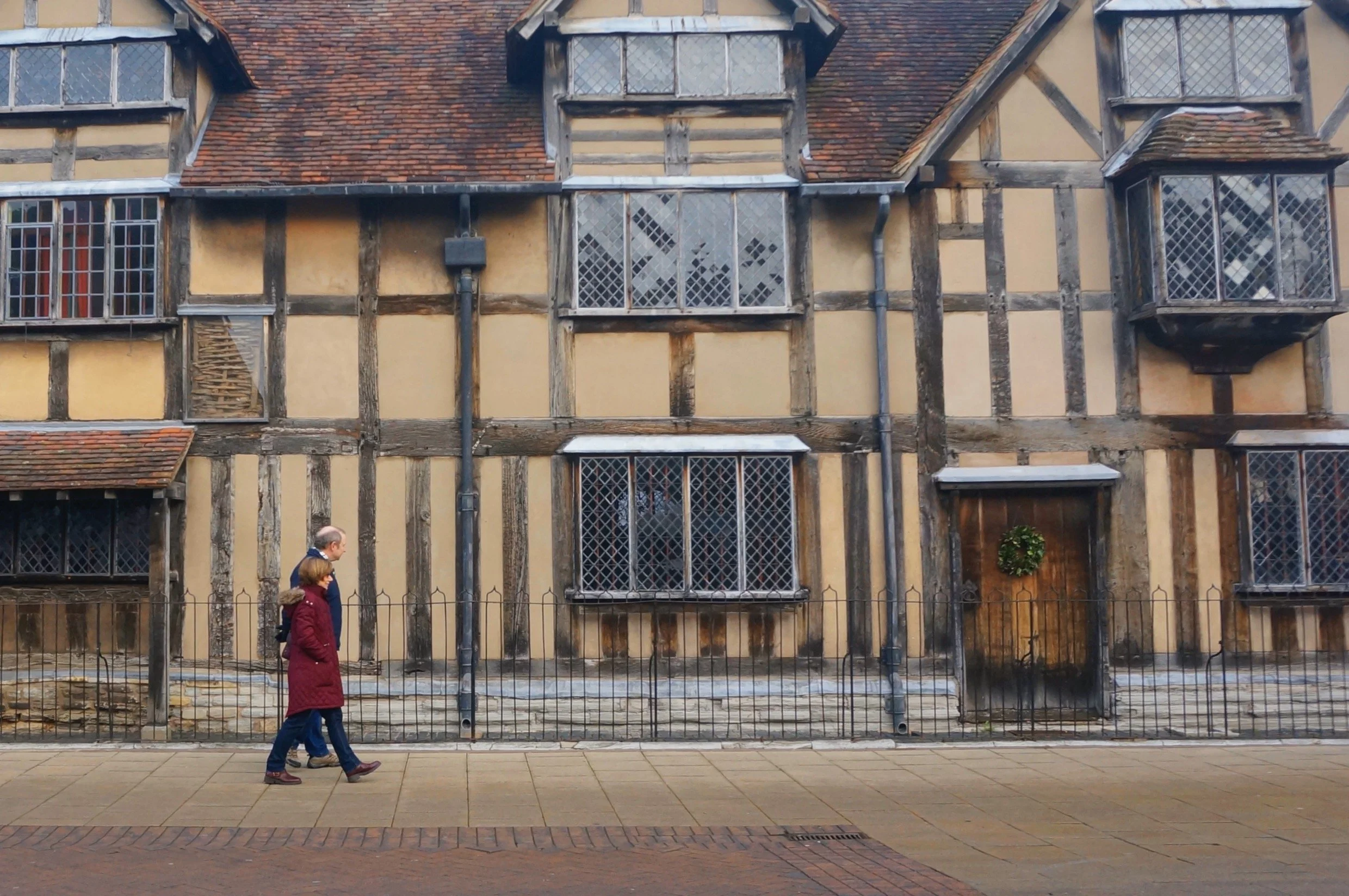 Two people walking past a historic timber-framed building with latticed windows.