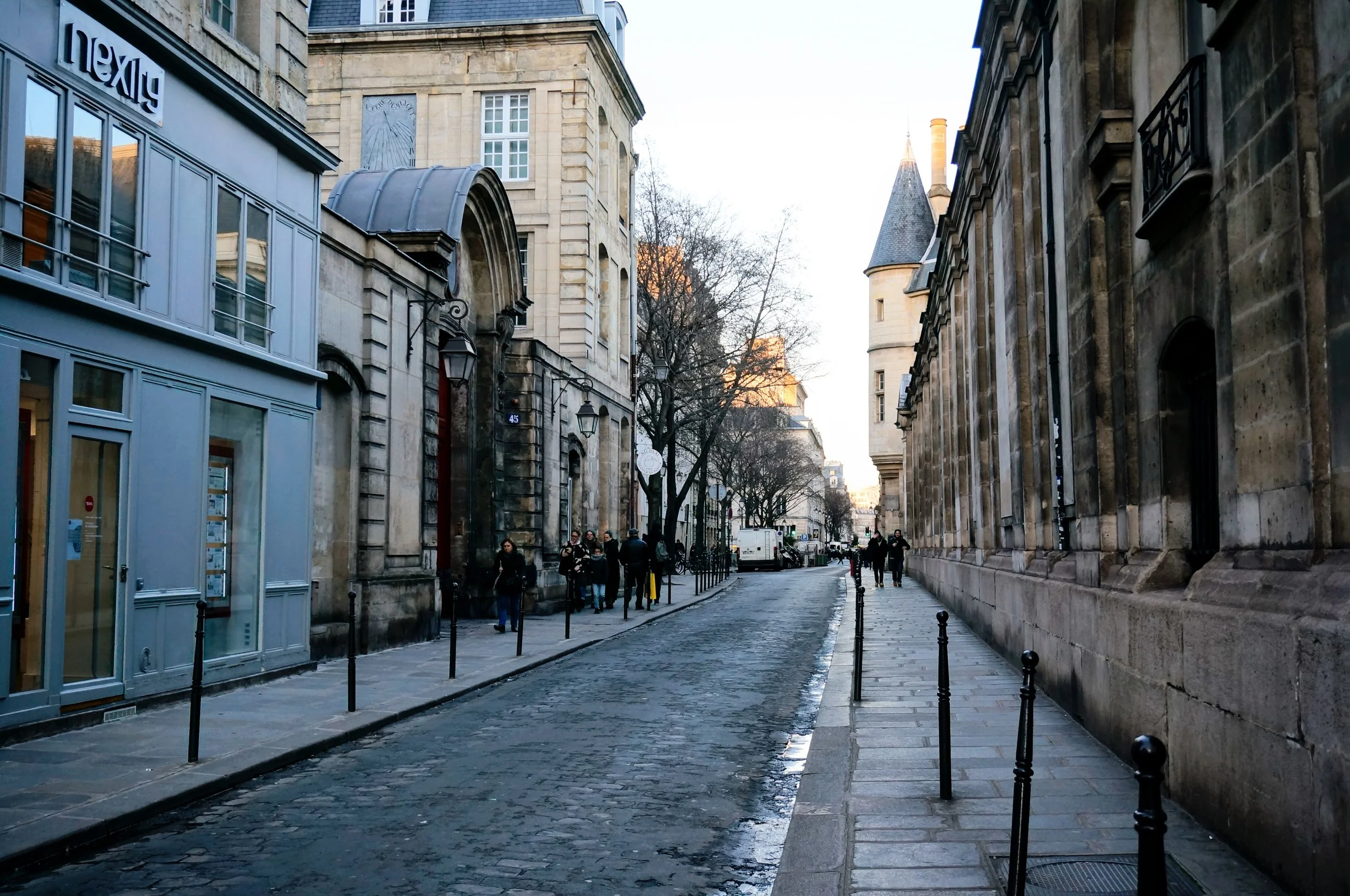 Street scene in Paris with historic buildings, pedestrians, and cobblestone road.