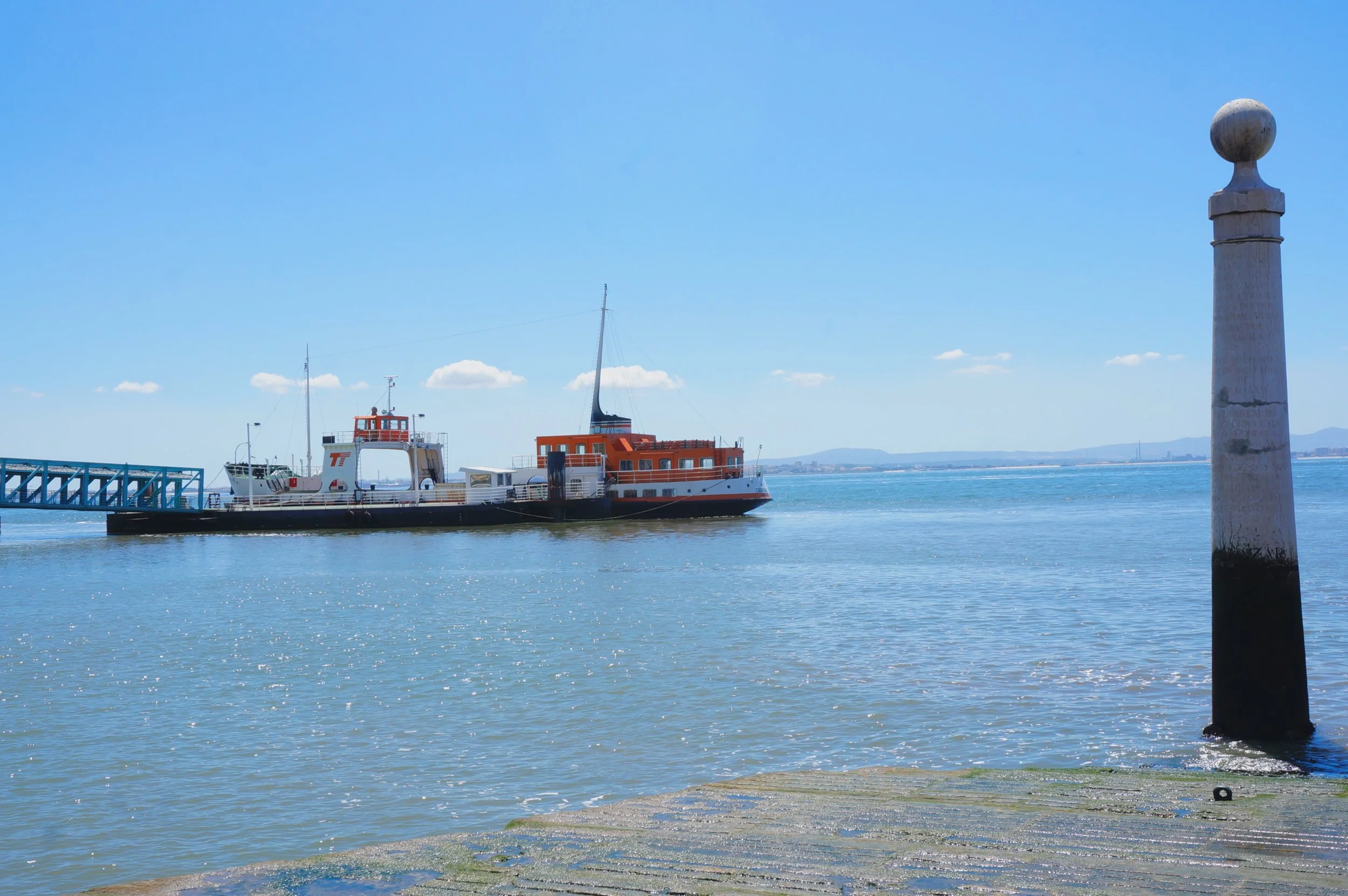 Photo taken by Christina Sarelakos of a ferry on water near a concrete pier with a round-topped post, under a clear blue sky.