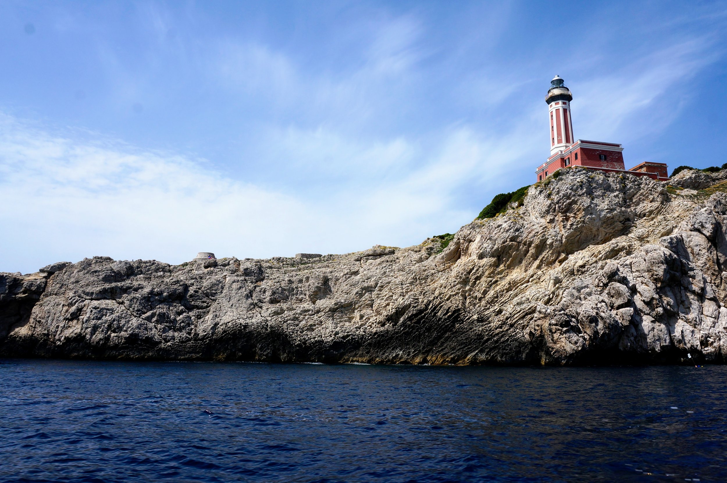 Lighthouse on rocky coastline with blue sky and ocean.